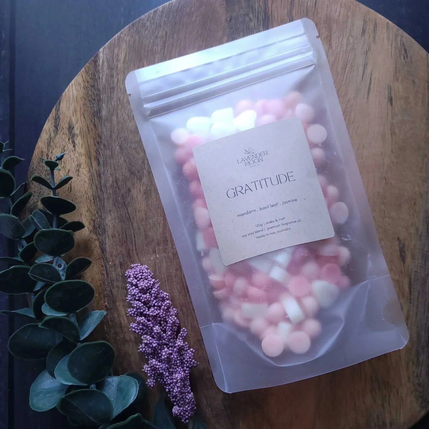 Gratitude Wax Melt with mandarin, basil leaf, and jasmine scents in a clear pouch on wooden table.