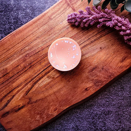 Vegan-friendly Dawnlight wax melt on wooden tray with purple flowers.