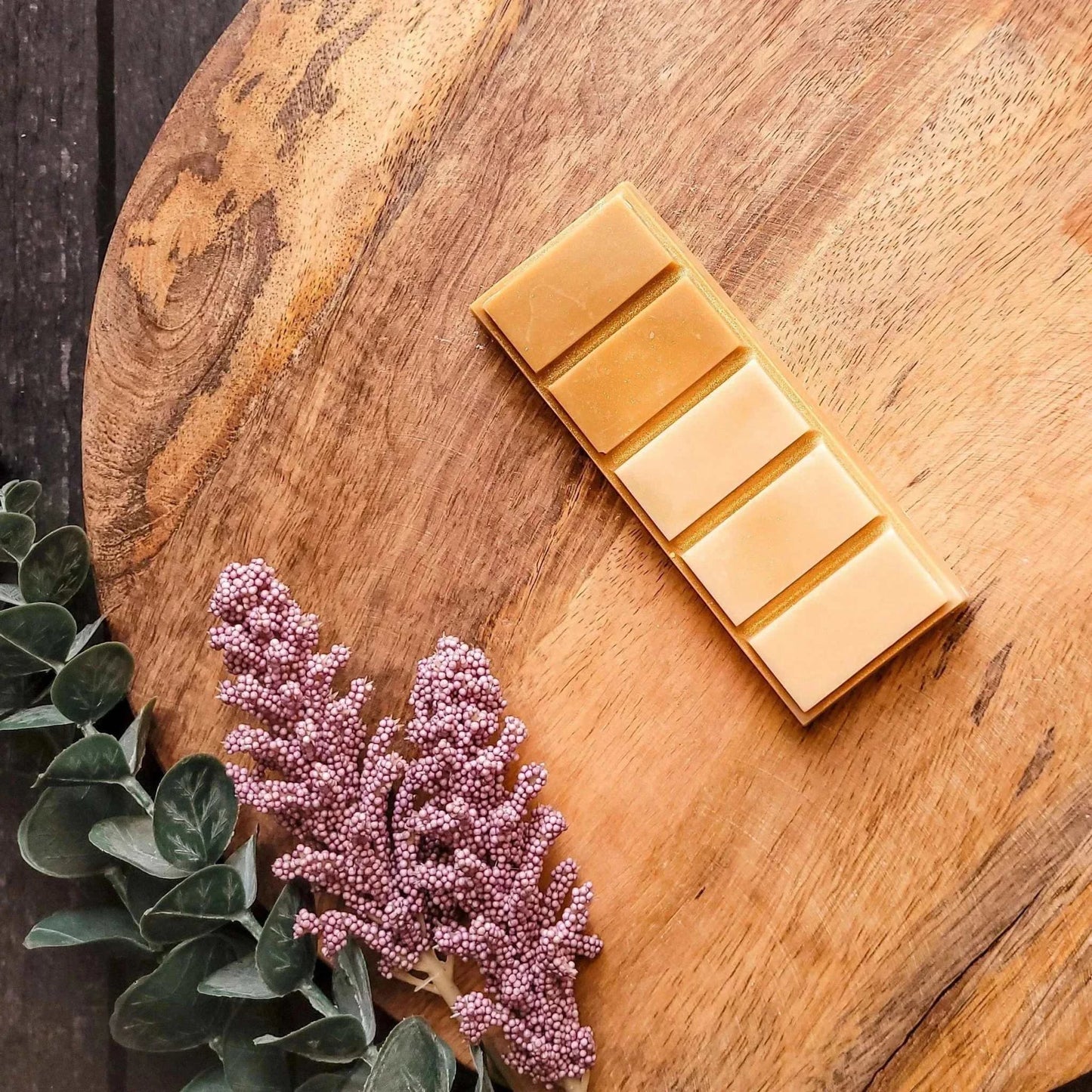 French Vanilla Bourbon wax melt with warm amber, orange, and vanilla scent on wooden surface with foliage.