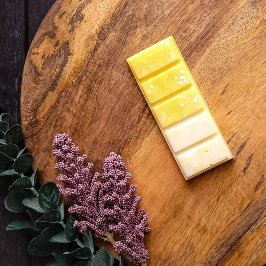 Lemon Meringue Waxmelt on wooden board with floral accents, featuring yellow and white sections made from vegan-friendly soy wax.