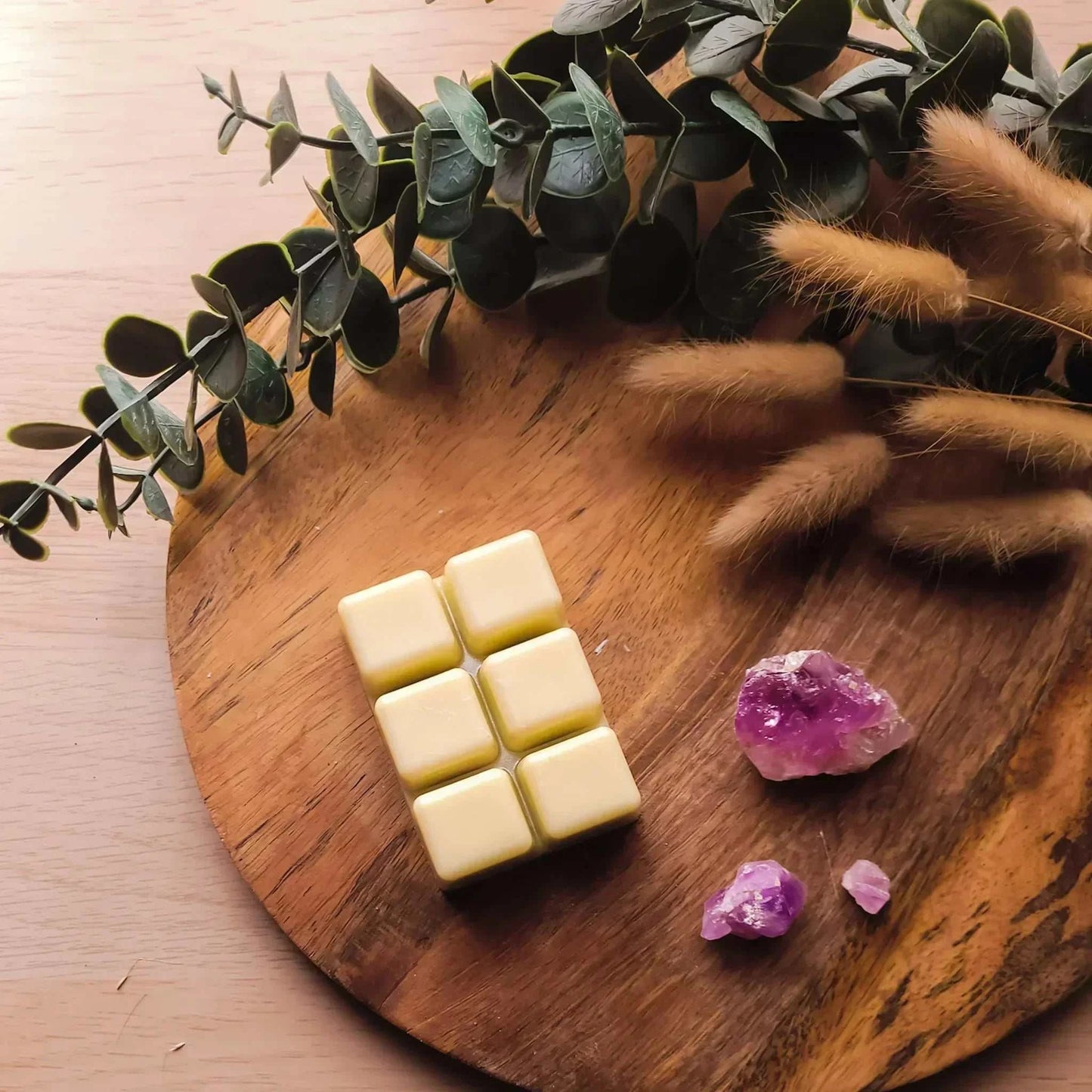 Vegan-friendly soy wax melts on a wooden board with green foliage.