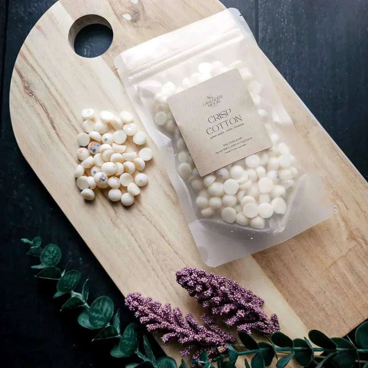 Crisp Cotton Waxmelt on wooden board with foliage, featuring scent notes of green apple, cedar, and lavender.