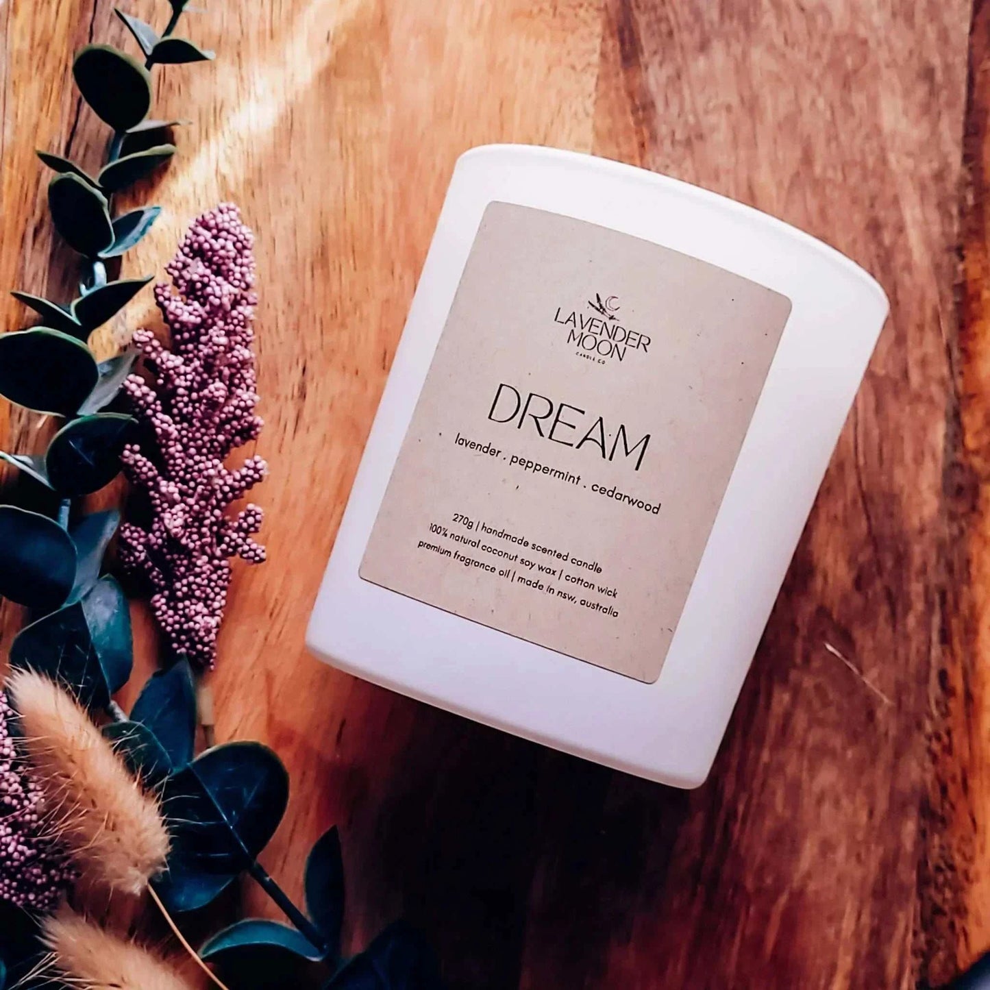 Dream Candle with lavender, mint, cedarwood blend on wooden surface with greenery.