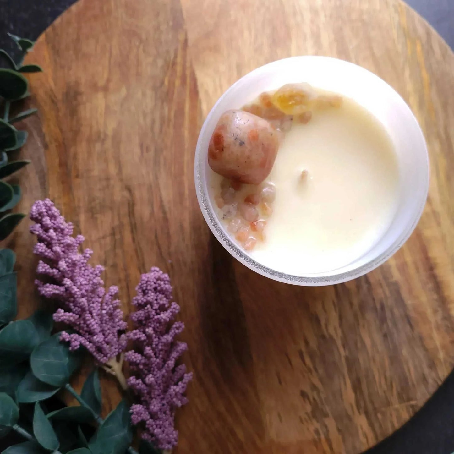 Glow Candle from Wellness Range with grapefruit, chamomile, and sandalwood aroma, adorned with sunstone chips, on a wooden surface.
