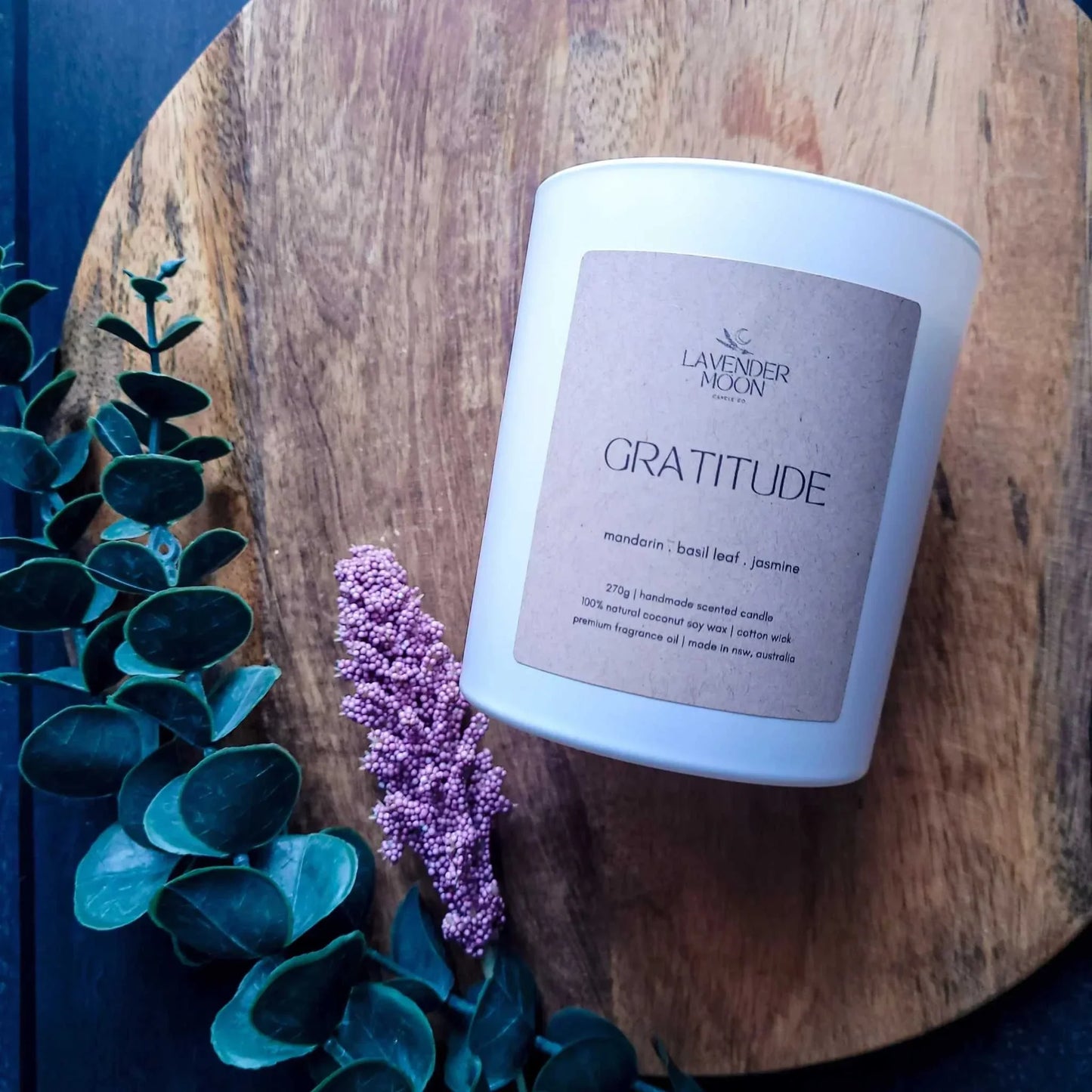 Gratitude Candle with mandarin, basil leaf, and jasmine scent on wooden board, part of vegan-friendly wellness range.