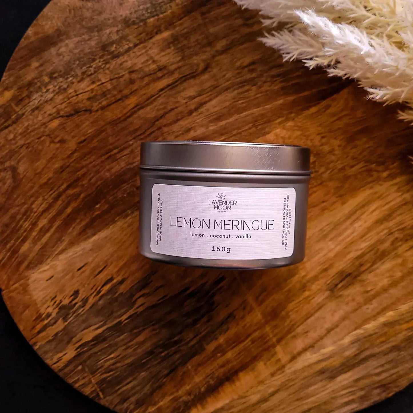 Lemon Meringue Candle with scents of lemon, coconut, and vanilla in a silver tin on a wooden surface.