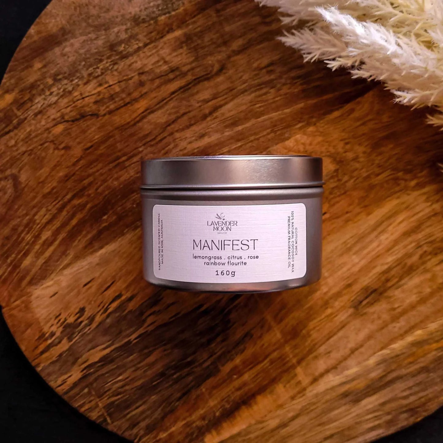Manifest Candle in tin on wooden surface, featuring lemongrass, citrus, and rose scents for wellness.