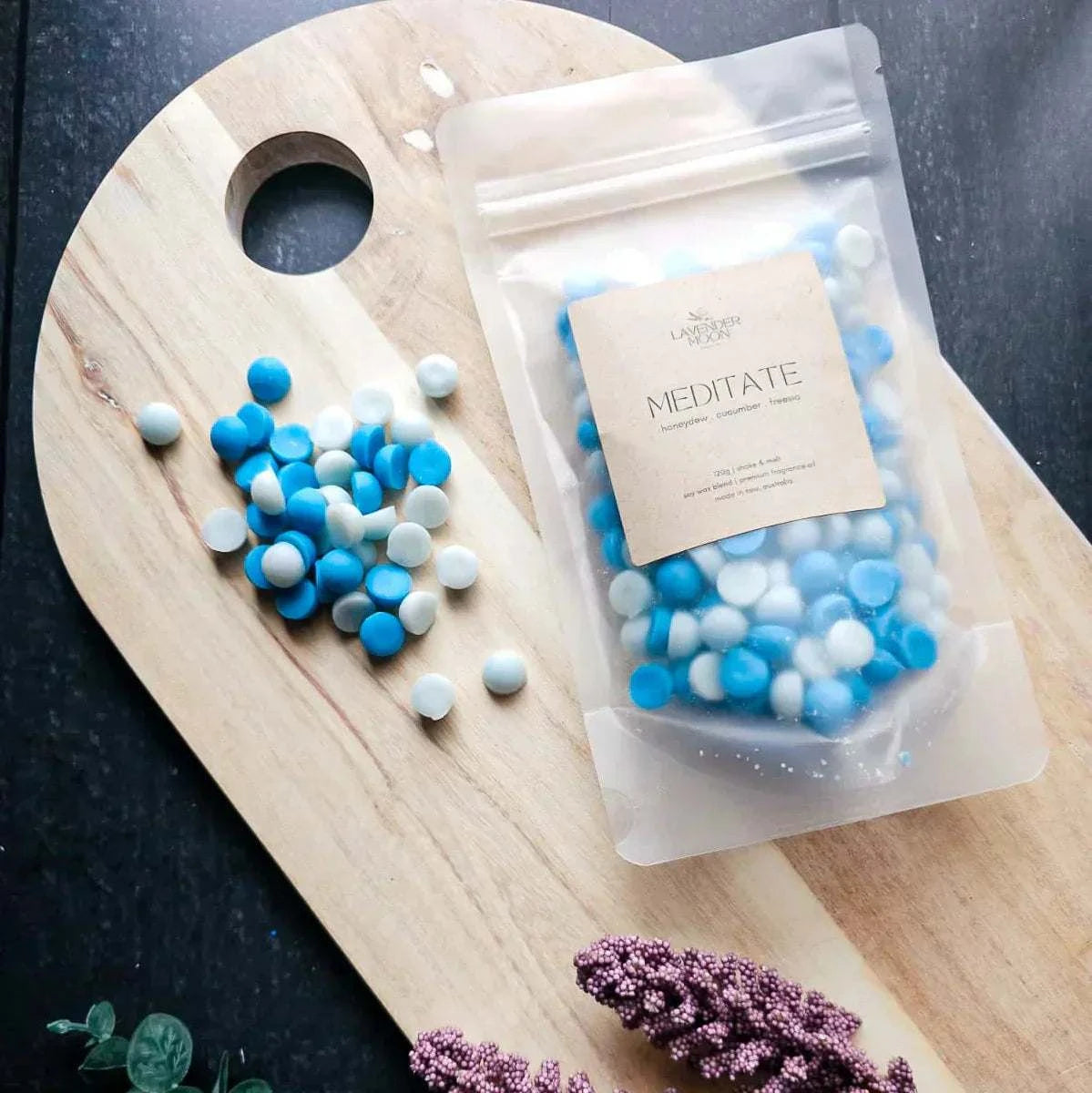 Meditate Waxmelt in pouch on wooden board, featuring blue and white pieces; honeydew, cucumber, and freesia scent.