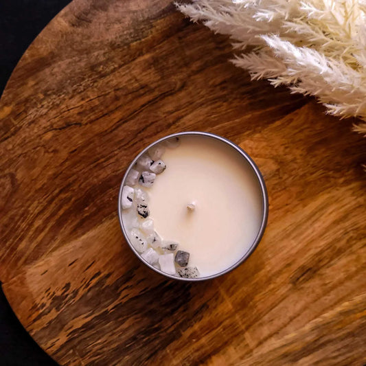 Meditate Candle with honeydew, cucumber, freesia scents and Rainbow Moonstone chips on wooden surface.