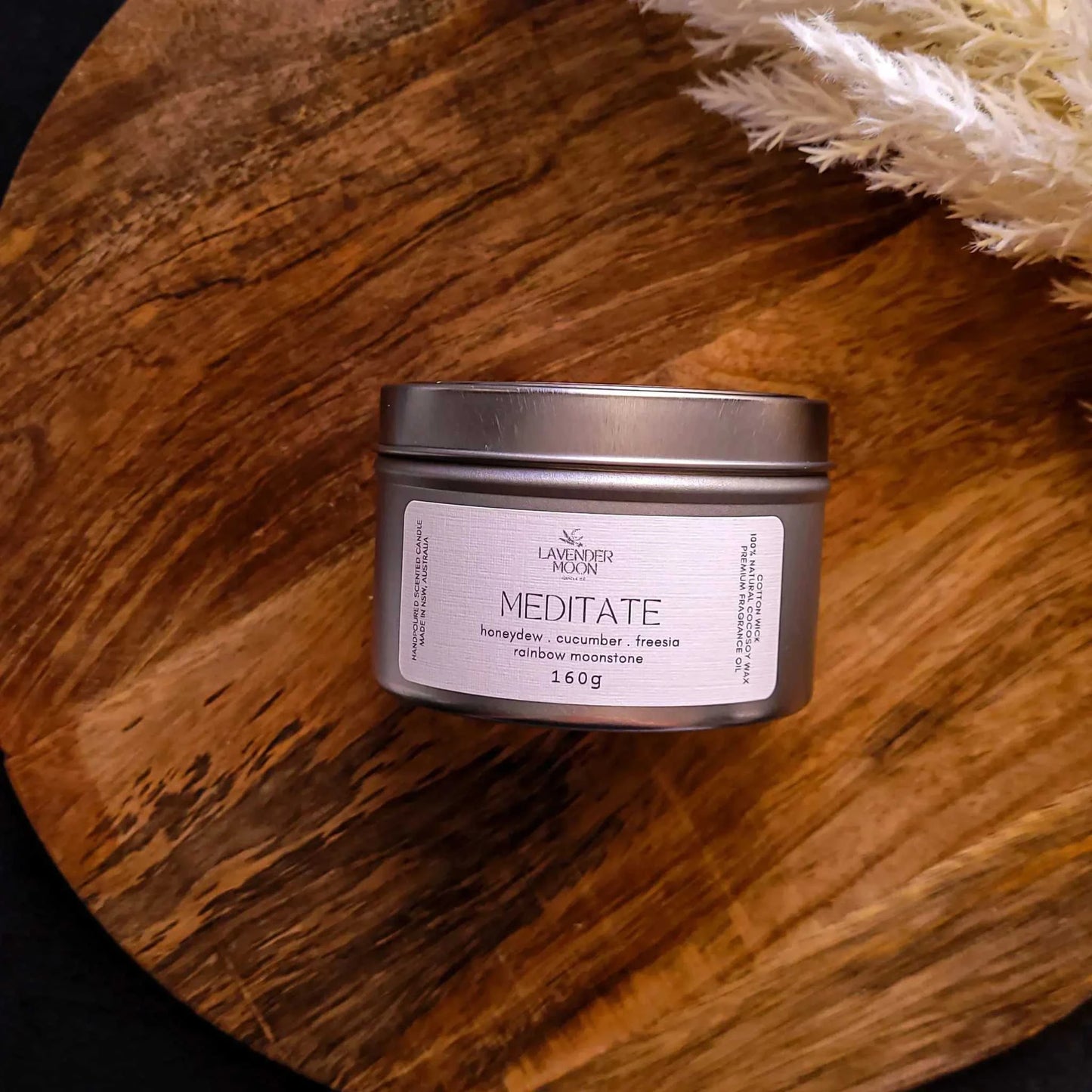 Meditate Candle with honeydew, cucumber, freesia, vegan coconut soy wax, rainbow moonstone, on a wooden surface.