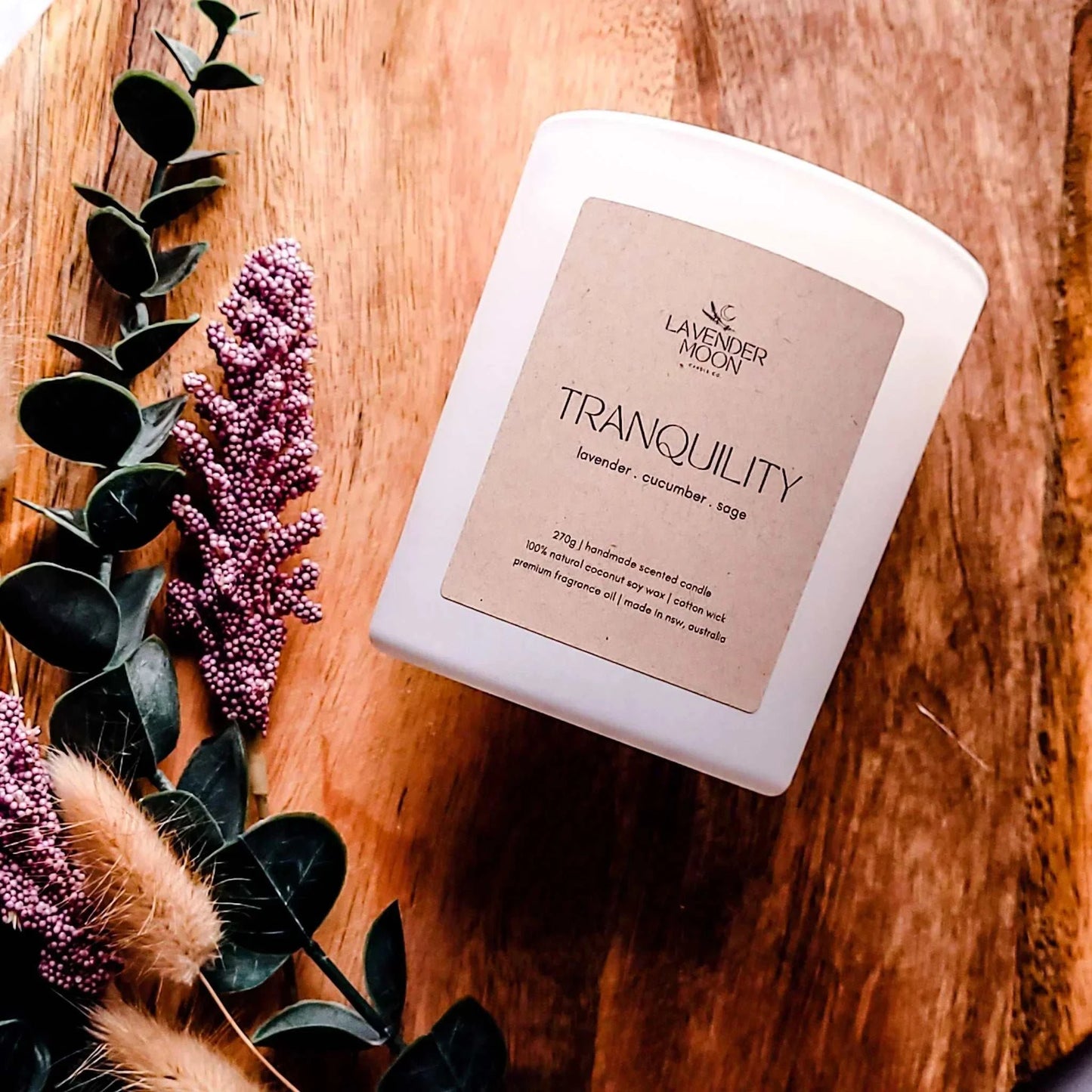 Tranquility Candle with lavender, cucumber, and sage on wooden surface with lavender sprigs.