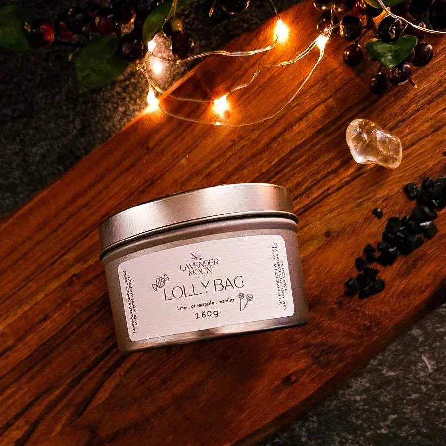 Lolly Bag 160g Candle Tin with lime, pineapple, and vanilla scents on a wooden surface with festive lights.