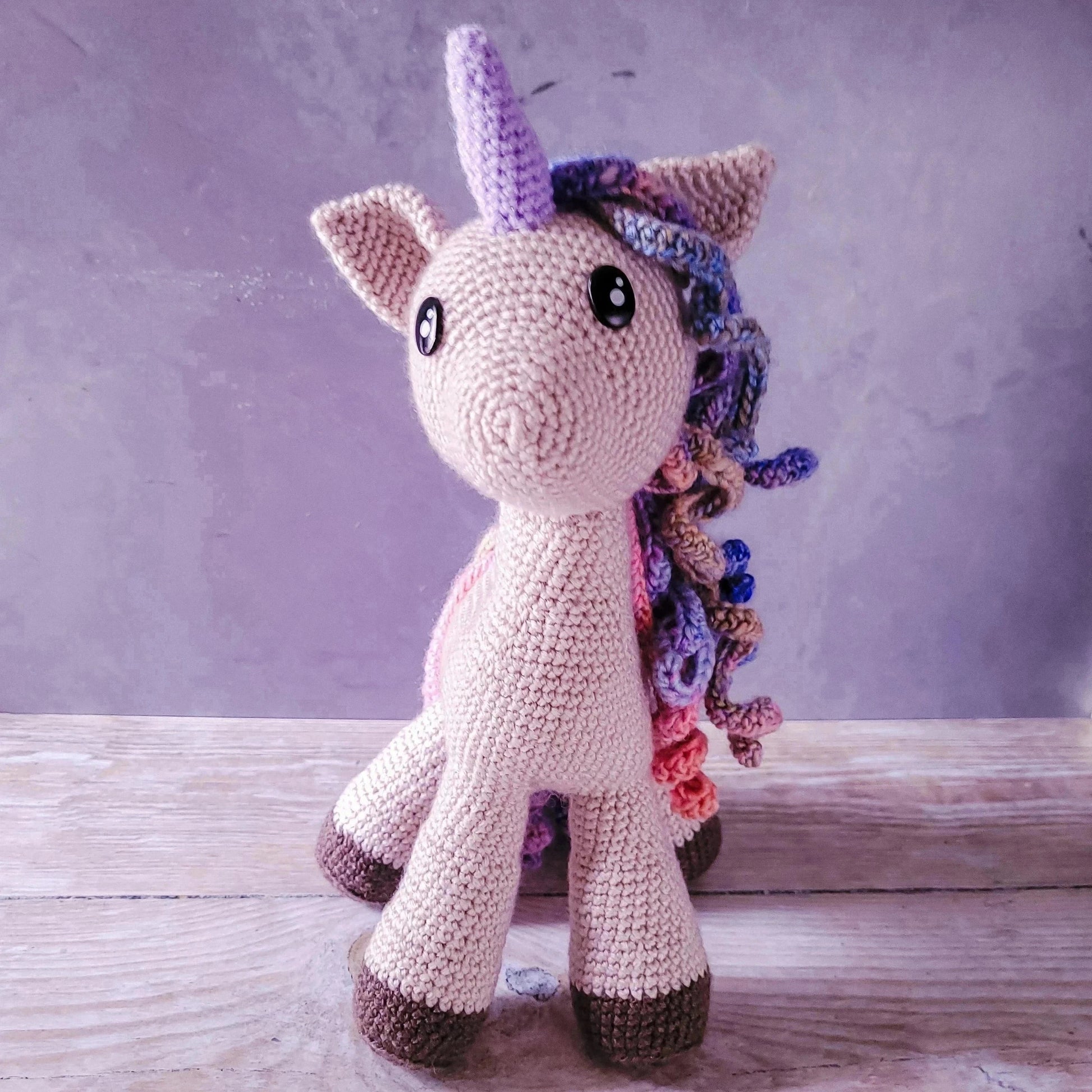 Hand-crocheted unicorn amigurumi soft toy with glittery lilac horn and vibrant colorful mane.